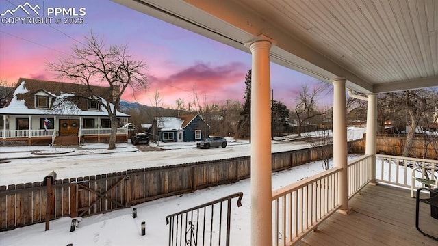 snow covered deck featuring covered porch and fence