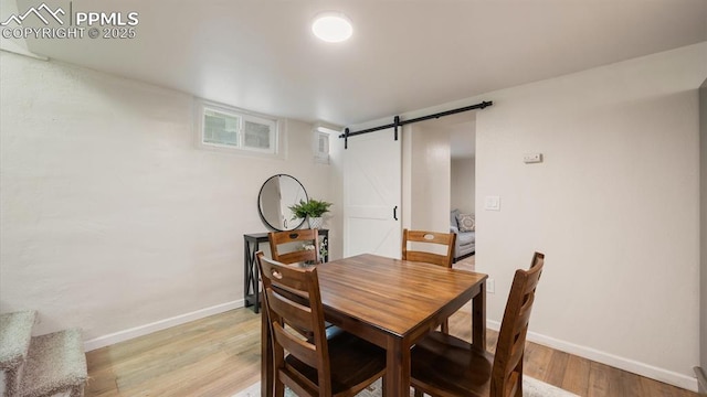 dining area with baseboards, light wood-style floors, and a barn door