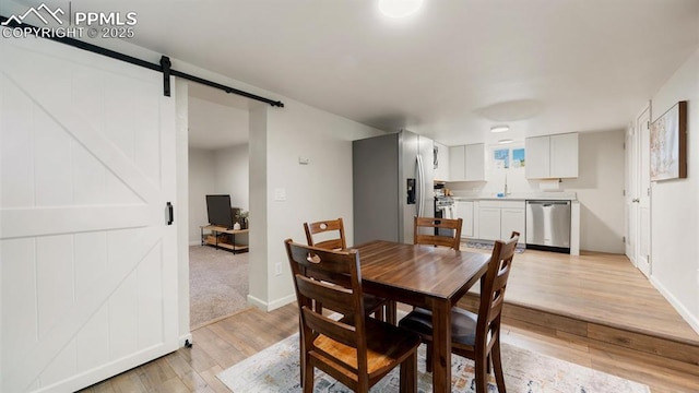 dining space with a barn door, baseboards, and light wood-type flooring