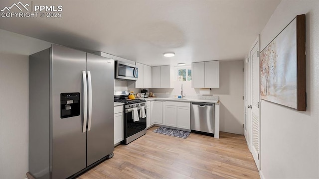 kitchen with light wood-style flooring, a sink, stainless steel appliances, light countertops, and white cabinets