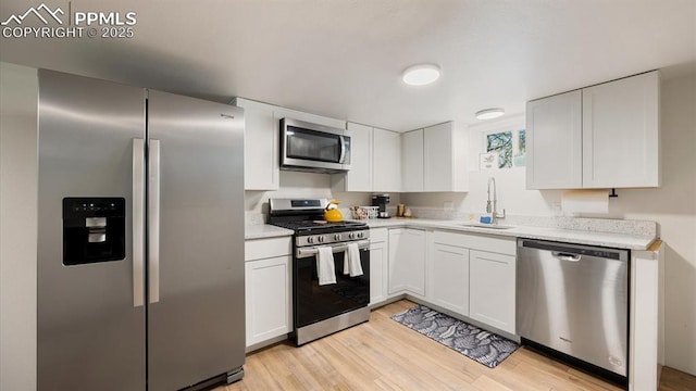 kitchen featuring light wood-type flooring, a sink, white cabinetry, appliances with stainless steel finishes, and light stone countertops