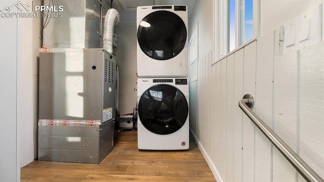 laundry room with heating unit, wood finished floors, laundry area, and stacked washer / dryer