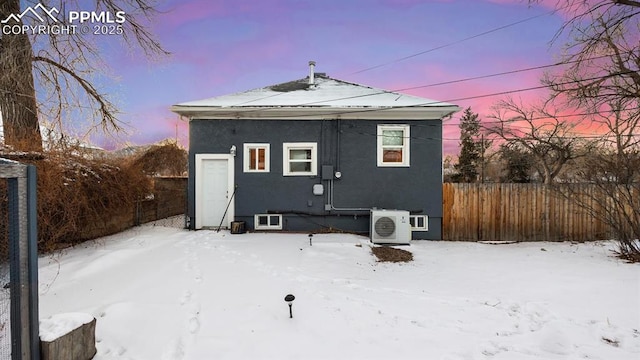 snow covered back of property featuring ac unit, stucco siding, and fence