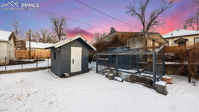 snow covered structure featuring an outdoor structure and fence