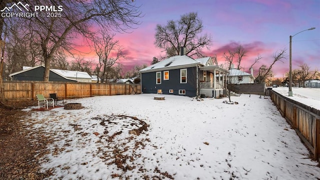 snow covered back of property with a fenced backyard and an outdoor fire pit