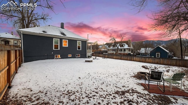 snow covered back of property with a fenced backyard and a chimney