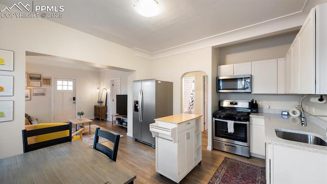 kitchen featuring a center island, light stone countertops, appliances with stainless steel finishes, wood finished floors, and white cabinetry