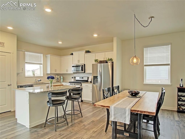 kitchen with hanging light fixtures, a kitchen island, appliances with stainless steel finishes, white cabinets, and light wood-type flooring