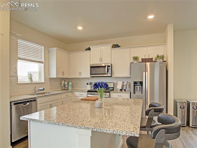 kitchen featuring white cabinets, appliances with stainless steel finishes, a kitchen island, and light stone counters