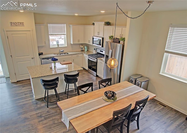 kitchen featuring light stone countertops, stainless steel appliances, sink, white cabinets, and a center island