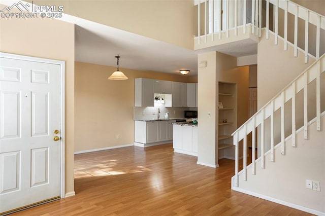 unfurnished living room with a towering ceiling, sink, and light wood-type flooring