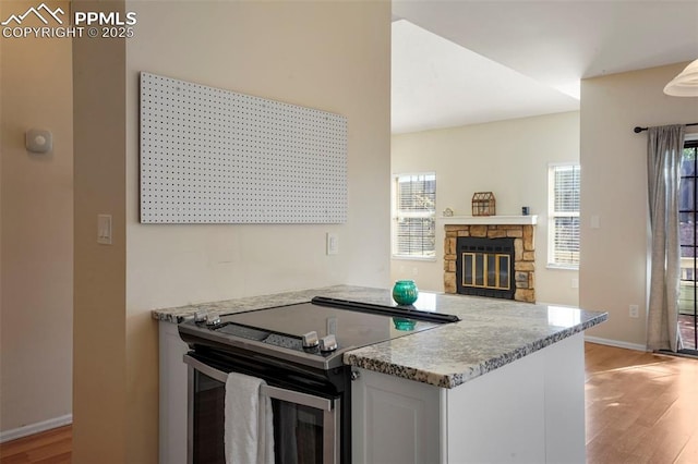 kitchen with white cabinetry, a stone fireplace, light hardwood / wood-style flooring, and stainless steel electric range