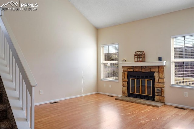 unfurnished living room featuring hardwood / wood-style flooring, a stone fireplace, and vaulted ceiling