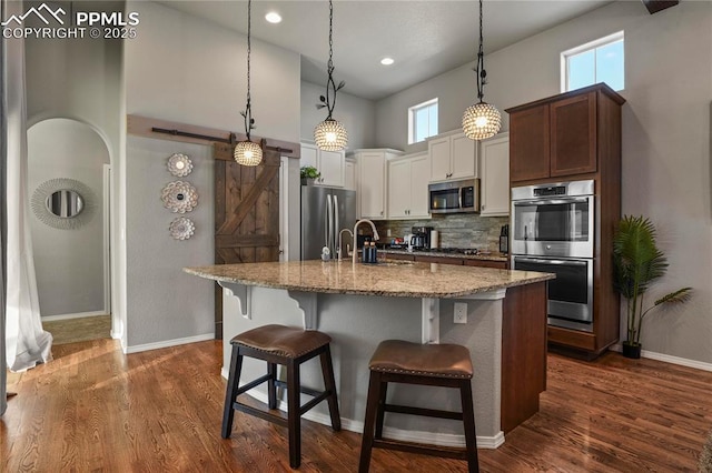 kitchen featuring appliances with stainless steel finishes, a towering ceiling, decorative backsplash, hanging light fixtures, and a breakfast bar