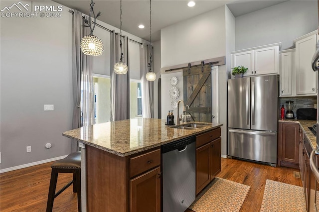 kitchen featuring white cabinets, stainless steel appliances, sink, a kitchen island with sink, and a barn door