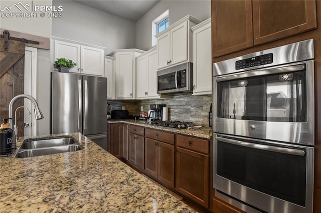 kitchen featuring white cabinetry, stainless steel appliances, sink, light stone counters, and a barn door