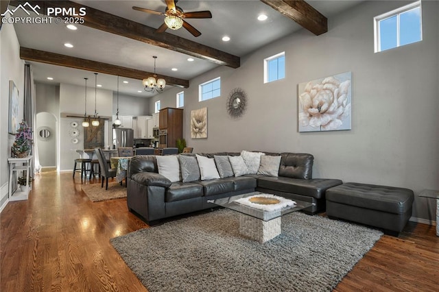 living room featuring ceiling fan with notable chandelier, a wealth of natural light, dark hardwood / wood-style flooring, and beam ceiling