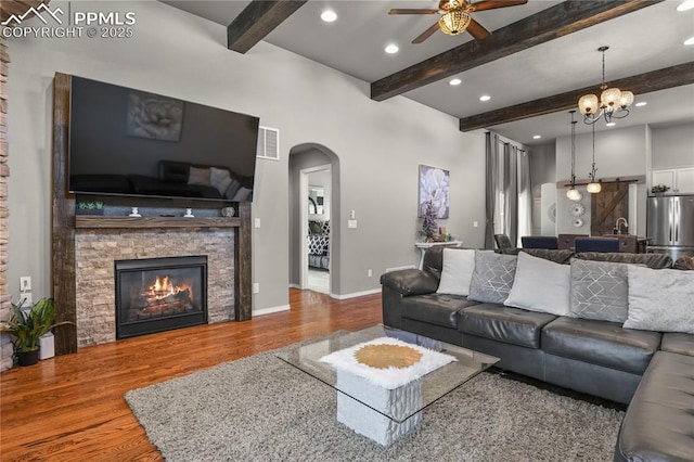 living room with ceiling fan with notable chandelier, wood-type flooring, beamed ceiling, and a fireplace