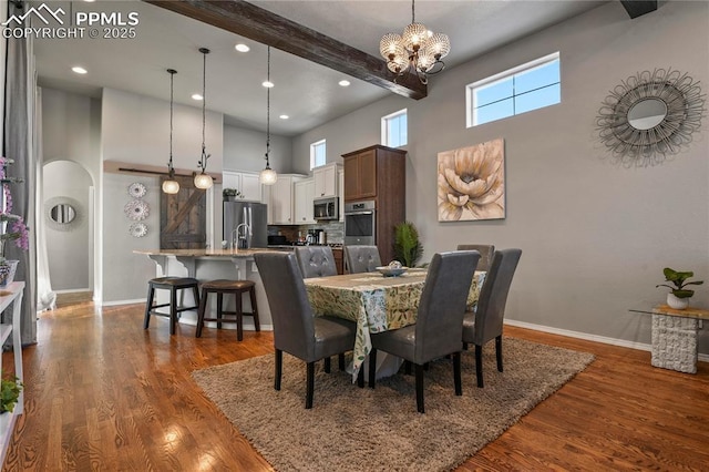 dining room featuring dark hardwood / wood-style floors, beamed ceiling, a high ceiling, and a chandelier