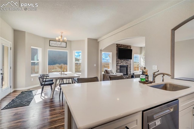 kitchen featuring white cabinetry, sink, stainless steel dishwasher, dark hardwood / wood-style floors, and a fireplace