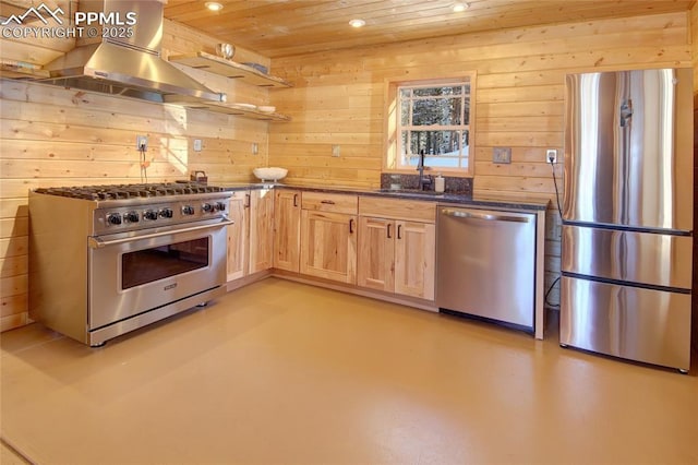 kitchen featuring light brown cabinetry, stainless steel appliances, wall chimney exhaust hood, and wood walls