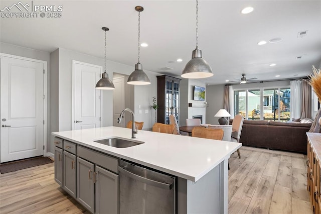 kitchen featuring ceiling fan, pendant lighting, stainless steel dishwasher, sink, and a kitchen island with sink