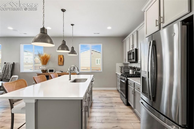 kitchen featuring stainless steel appliances, an island with sink, sink, gray cabinets, and a breakfast bar area