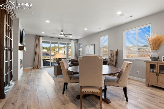 dining area featuring ceiling fan, a fireplace, and light hardwood / wood-style flooring