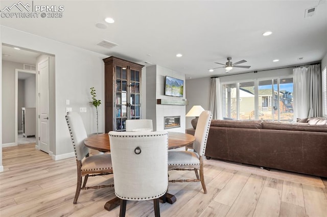 dining area with ceiling fan, light hardwood / wood-style flooring, and a tiled fireplace