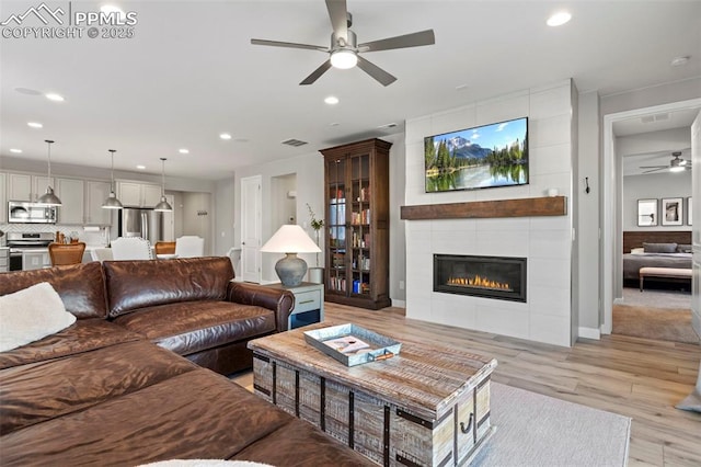 living room featuring light hardwood / wood-style floors, a tile fireplace, and ceiling fan