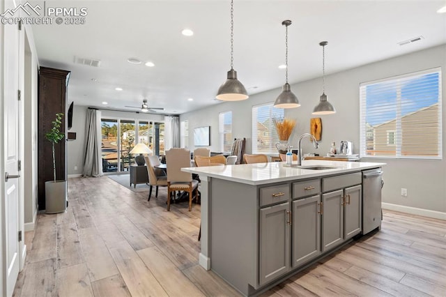 kitchen with pendant lighting, dishwasher, an island with sink, sink, and gray cabinetry