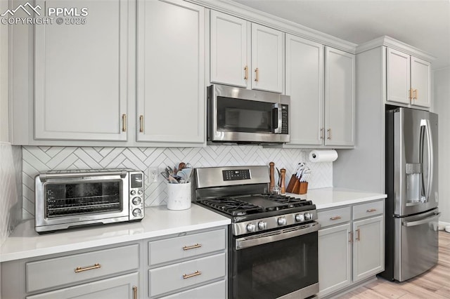 kitchen featuring backsplash, light wood-type flooring, appliances with stainless steel finishes, and gray cabinetry