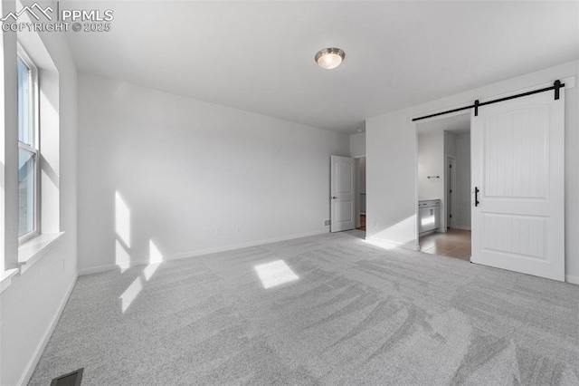 unfurnished bedroom with a barn door and light colored carpet