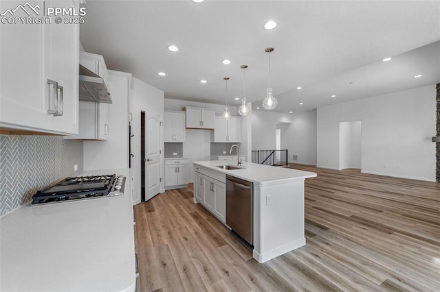 kitchen with appliances with stainless steel finishes, a kitchen island with sink, sink, white cabinets, and hanging light fixtures