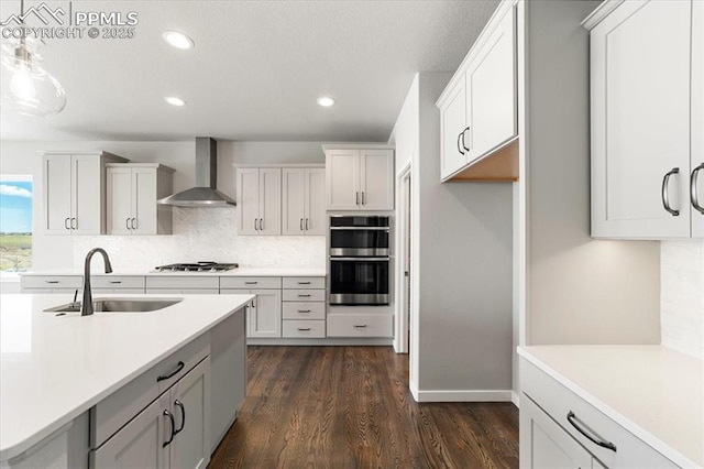 kitchen with white cabinetry, sink, stainless steel appliances, wall chimney range hood, and decorative light fixtures