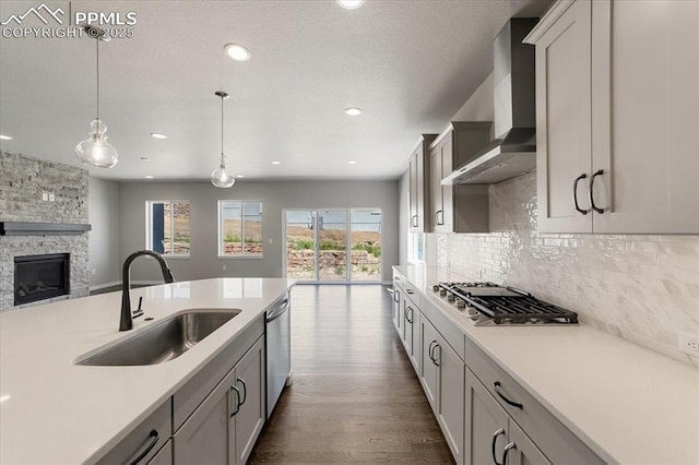 kitchen with pendant lighting, a stone fireplace, sink, wall chimney exhaust hood, and appliances with stainless steel finishes