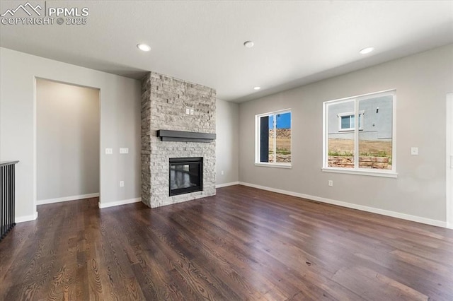 unfurnished living room with dark hardwood / wood-style flooring and a stone fireplace