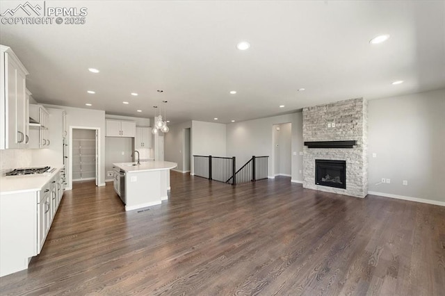 kitchen with a fireplace, hanging light fixtures, dark wood-type flooring, and an island with sink