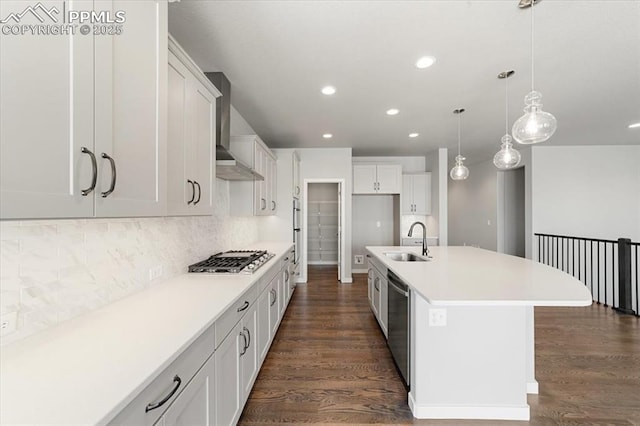 kitchen with stainless steel appliances, a kitchen island with sink, wall chimney range hood, sink, and white cabinets