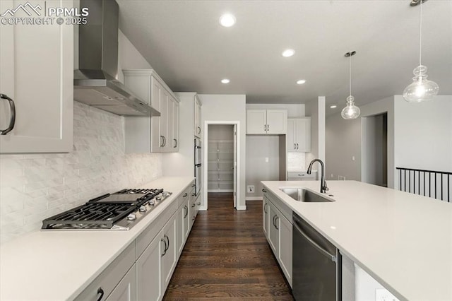 kitchen featuring appliances with stainless steel finishes, sink, wall chimney range hood, decorative light fixtures, and white cabinetry