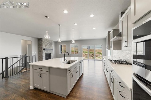 kitchen featuring sink, backsplash, decorative light fixtures, a kitchen island with sink, and appliances with stainless steel finishes