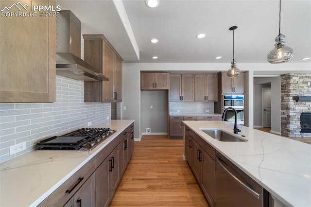 kitchen with appliances with stainless steel finishes, light stone counters, sink, wall chimney range hood, and pendant lighting