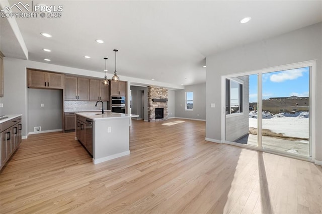 kitchen with sink, backsplash, pendant lighting, light hardwood / wood-style floors, and a kitchen island with sink