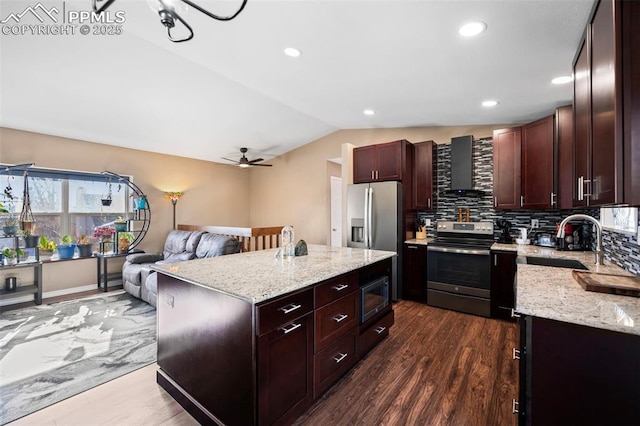 kitchen featuring appliances with stainless steel finishes, a center island, wall chimney range hood, vaulted ceiling, and sink