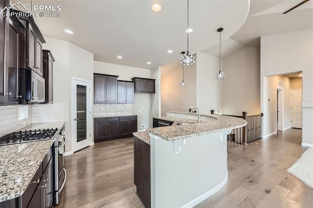 kitchen featuring light stone counters, hanging light fixtures, stainless steel appliances, decorative backsplash, and sink