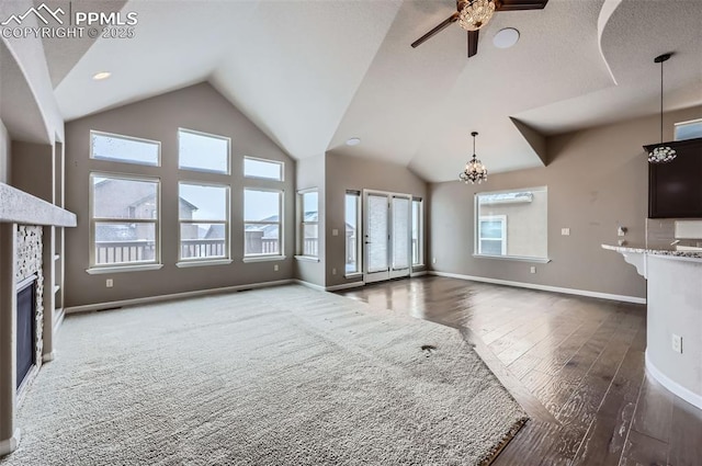 unfurnished living room featuring ceiling fan with notable chandelier, dark hardwood / wood-style flooring, a fireplace, and vaulted ceiling