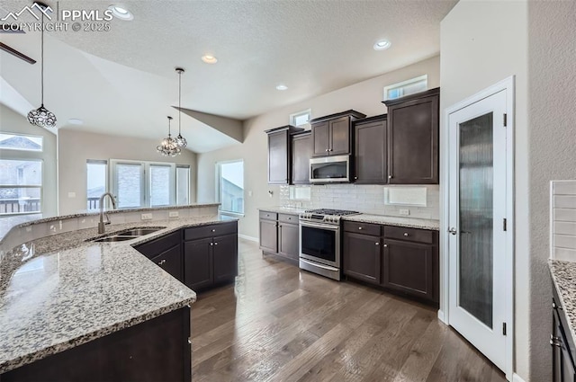 kitchen with sink, decorative light fixtures, vaulted ceiling, light stone countertops, and appliances with stainless steel finishes