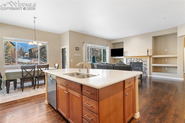 kitchen with pendant lighting, dishwasher, sink, built in features, and an island with sink