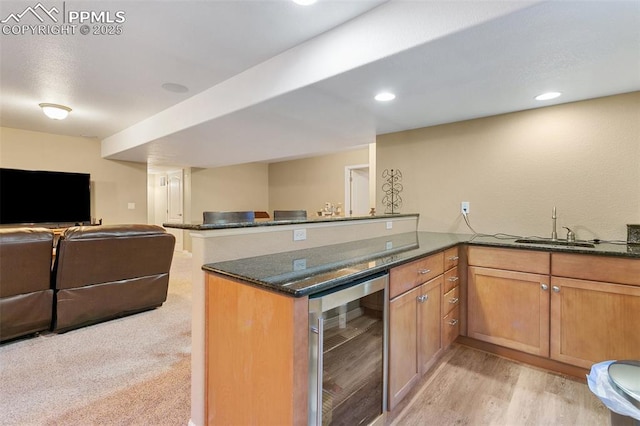 kitchen with sink, dark stone countertops, light colored carpet, kitchen peninsula, and beverage cooler