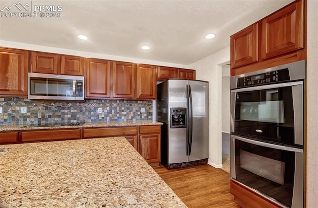 kitchen with stainless steel appliances, light hardwood / wood-style flooring, light stone counters, and tasteful backsplash